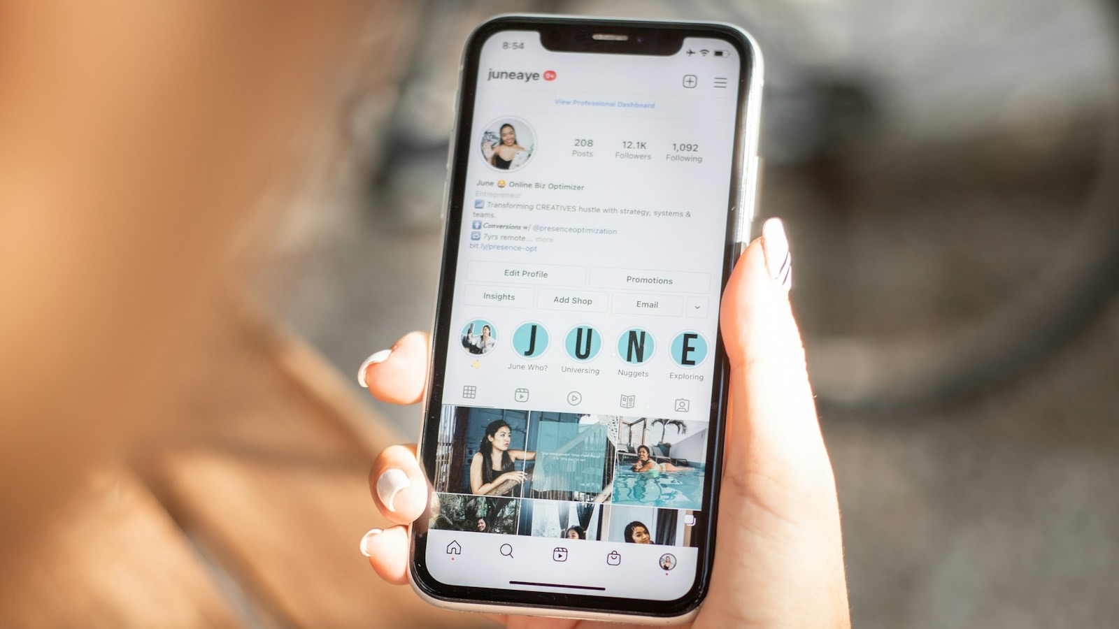 Main qui tient un smartphone affichant un profil Instagram professionnel, avec sa bio, ses stories et sa grille de photos