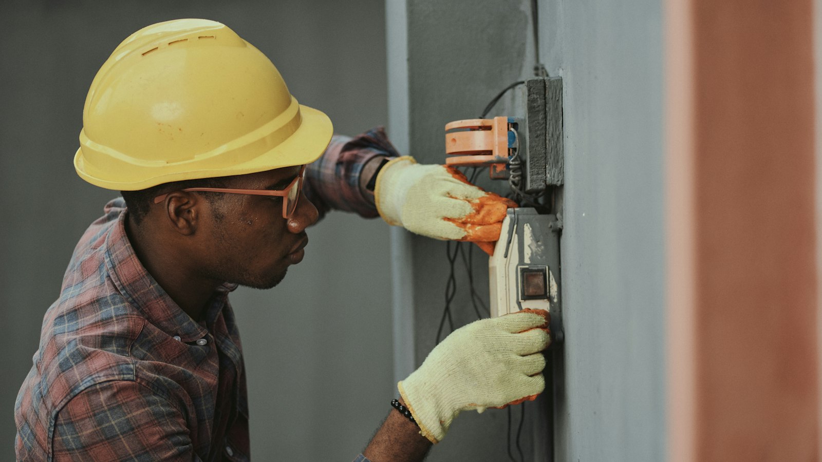 Électricien casqué et ganté qui intervient sur un boîtier électrique mural chez un client